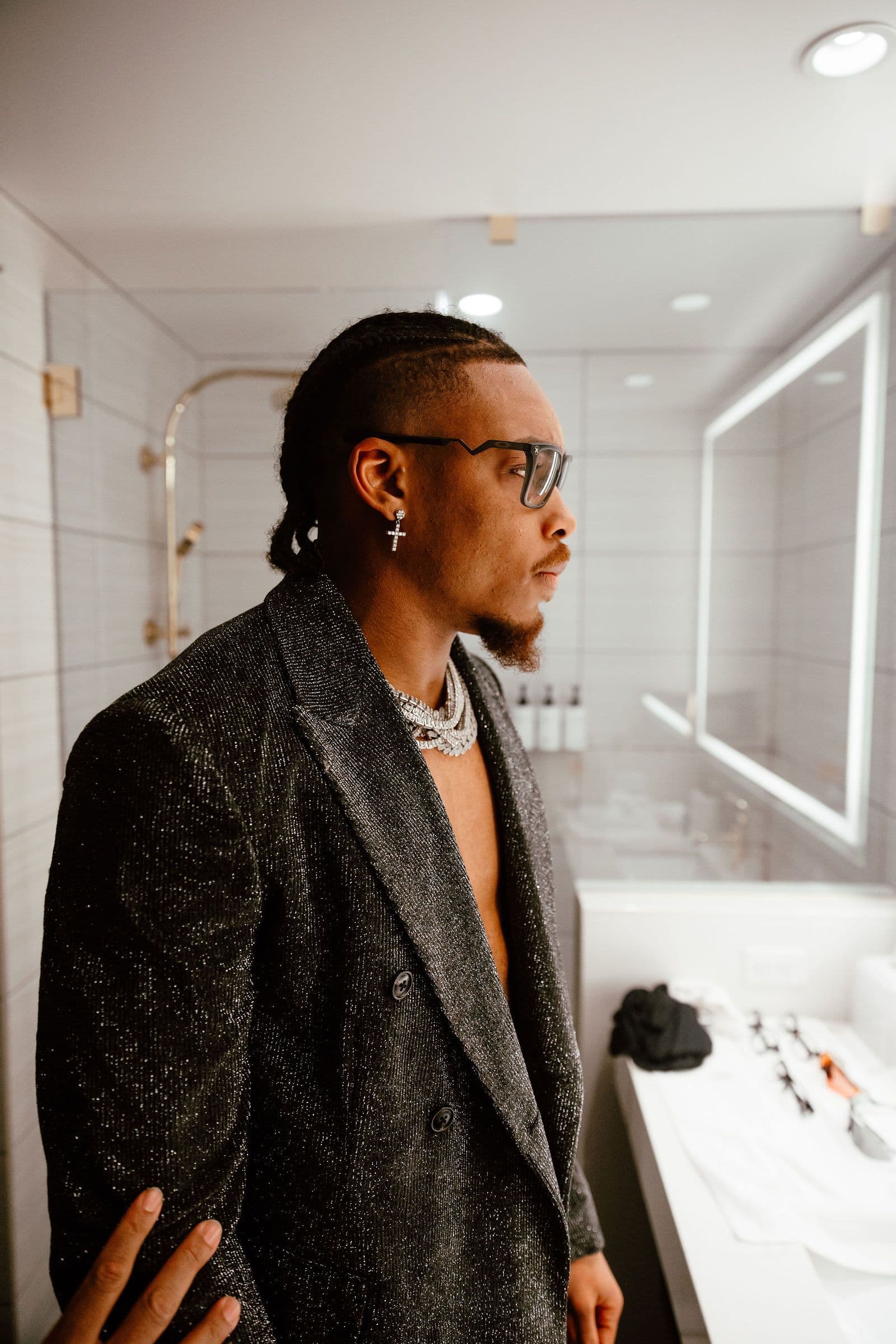 Justin Jefferson in a sparkly jacket and glasses, looking right in a bathroom