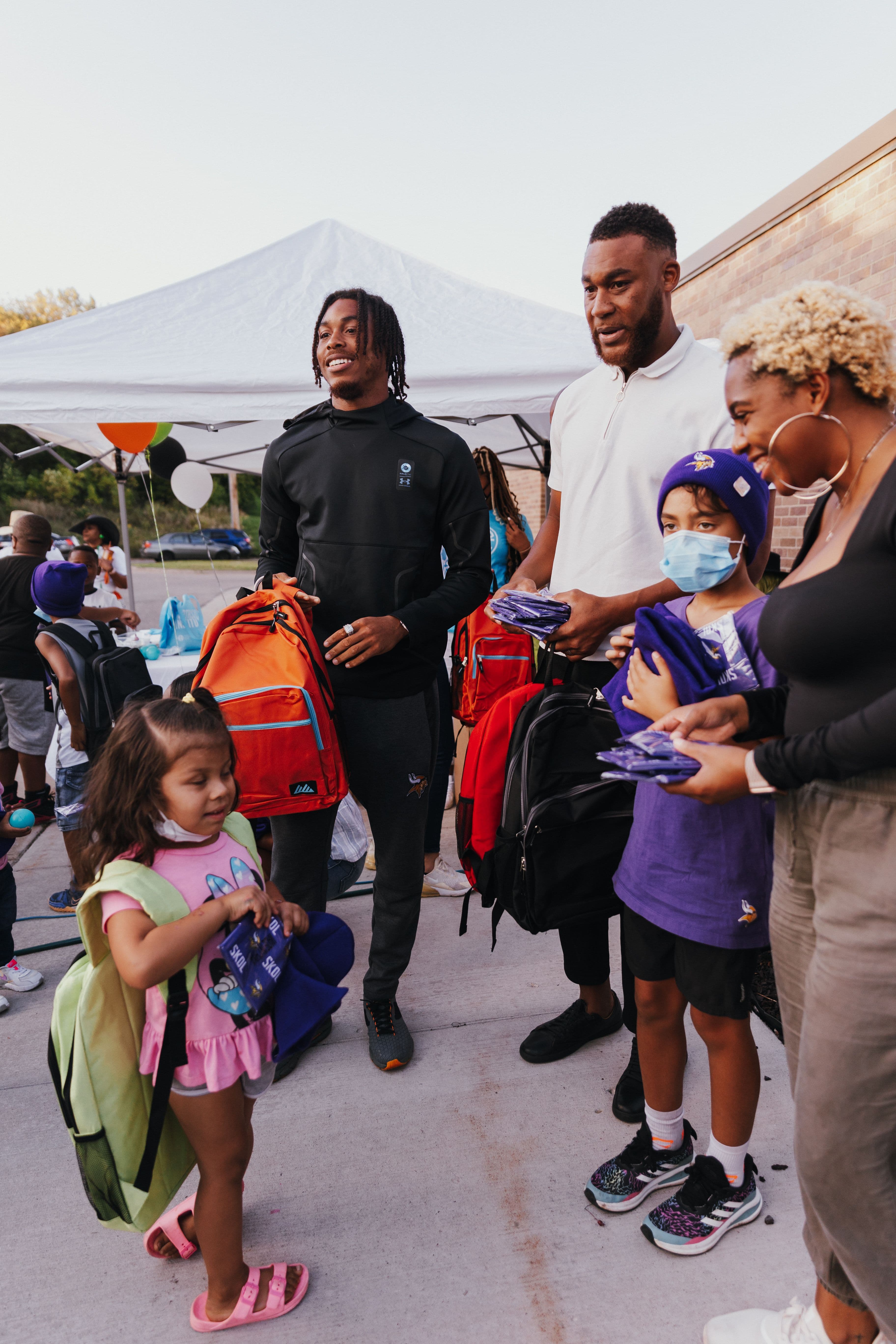 Justin Jefferson and a teammate handing out backpacks under the tent at the Backpack Drive