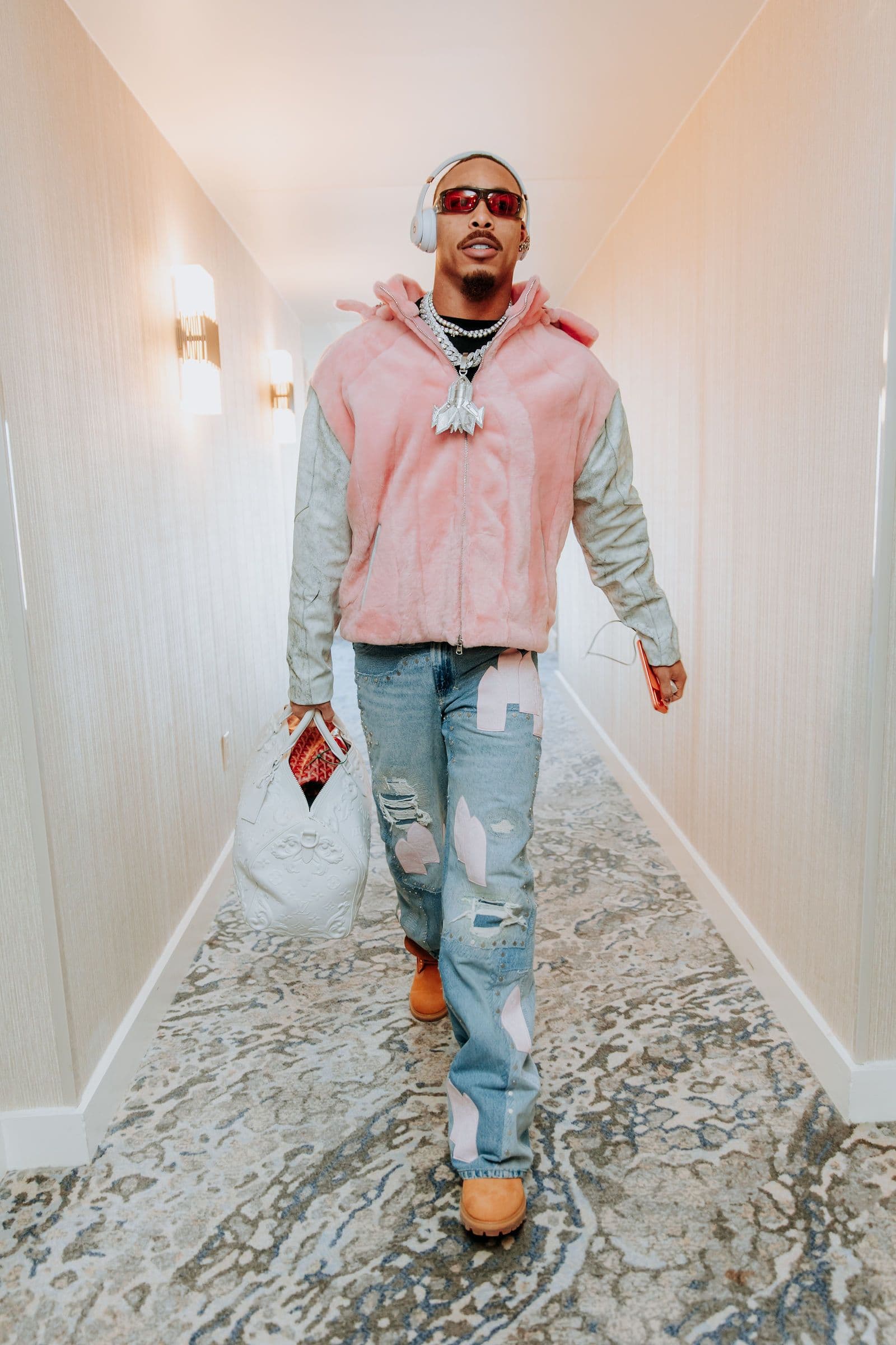 Justin Jefferson walks down a hallway wearing a pink jacket, ripped jeans, and sunglasses