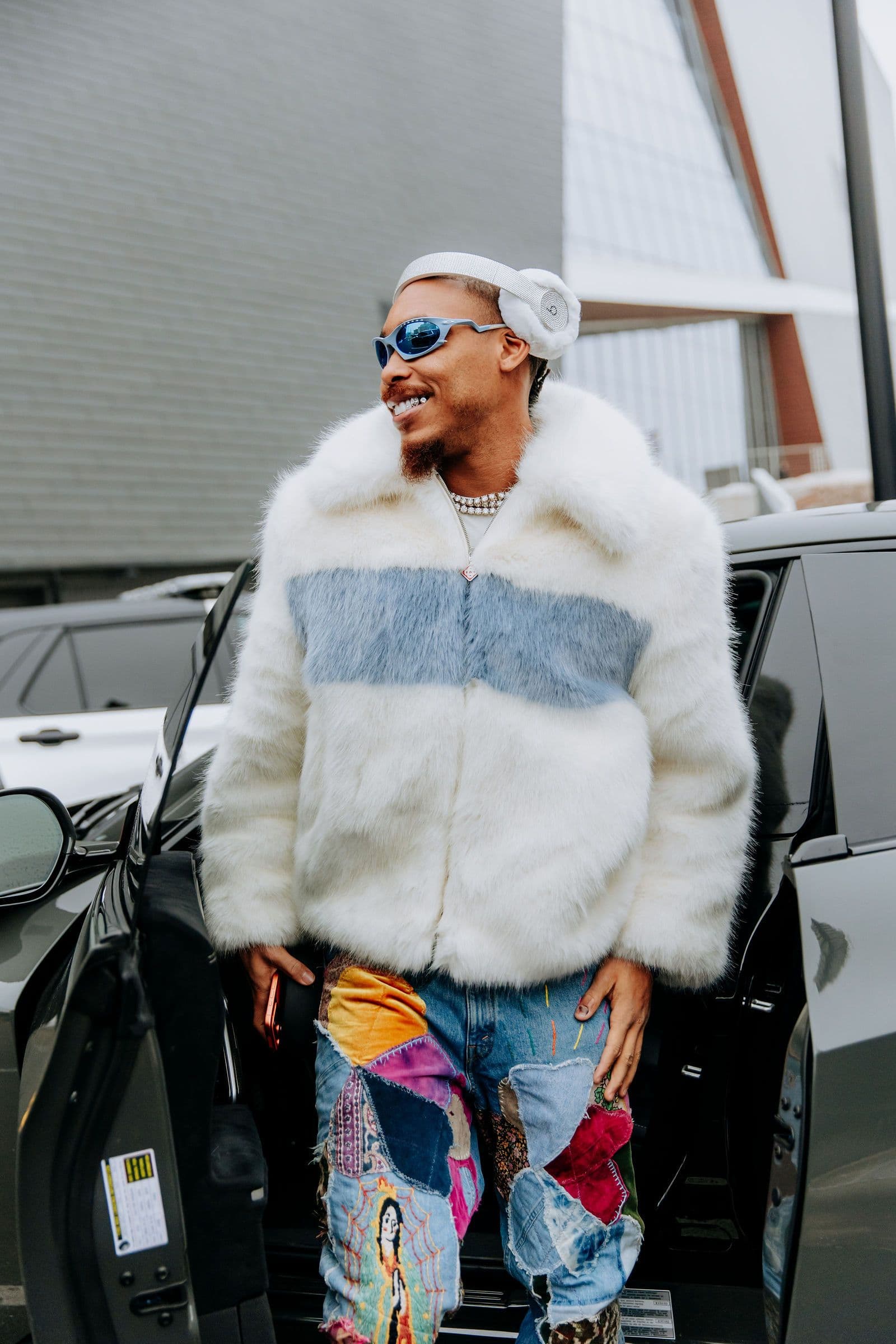 Justin Jefferson in a fur coat, sunglasses, and headphones, standing by a car
