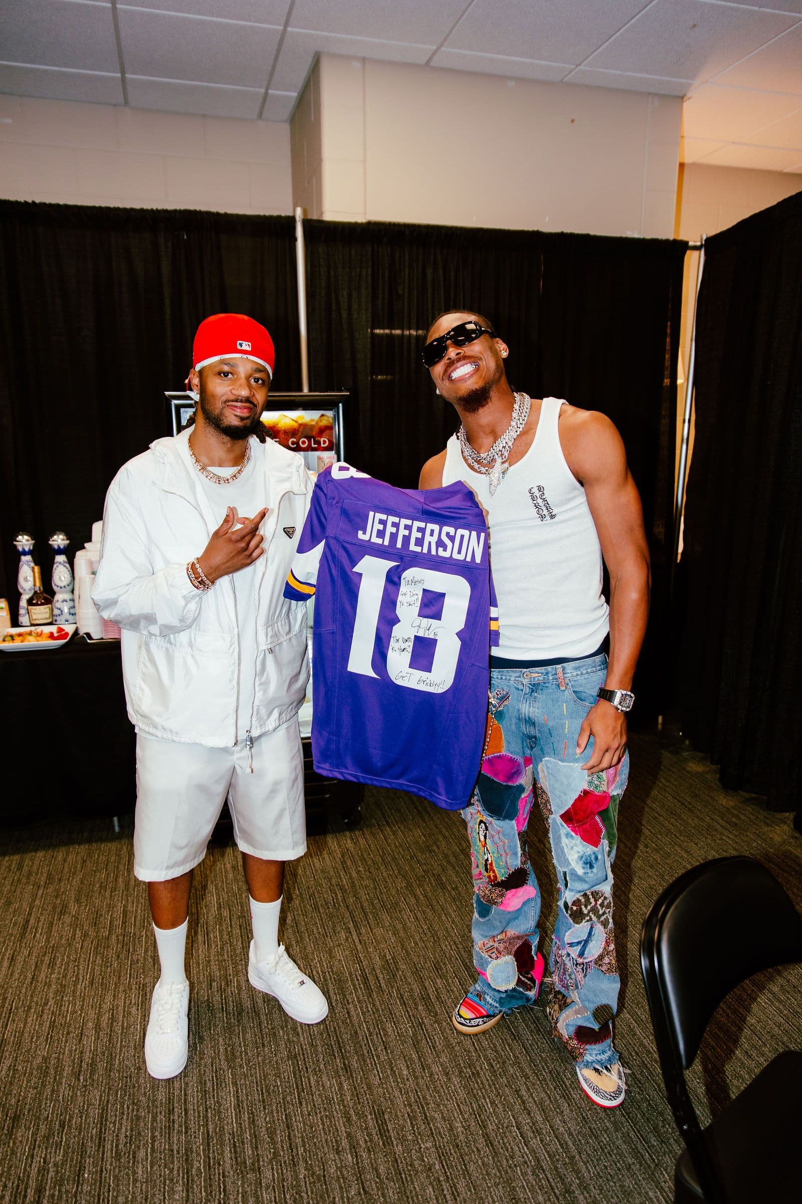Two men, one holding a purple Vikings jersey, pose indoors