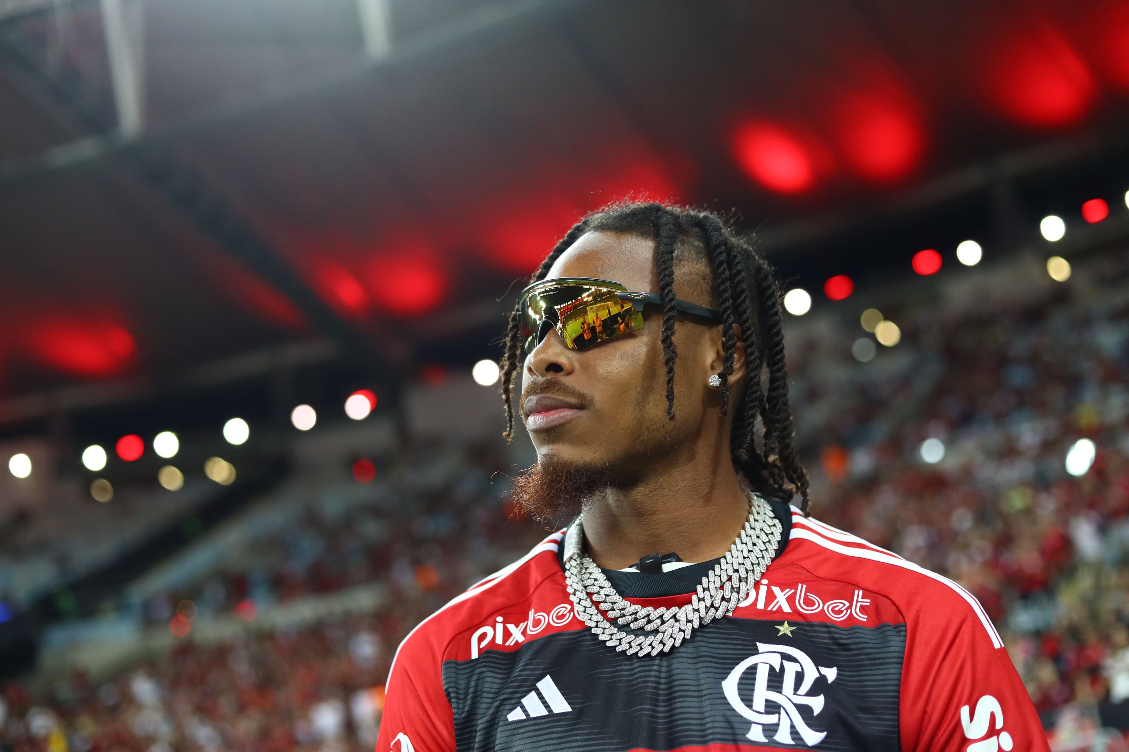 Justin Jefferson wears sunglasses and a red jersey in a stadium with blurred lights