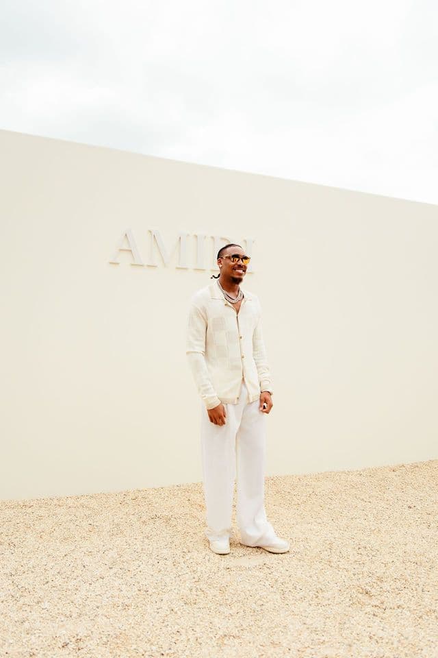 Justin Jefferson stands in front of a light-colored wall with text, wearing a white outfit