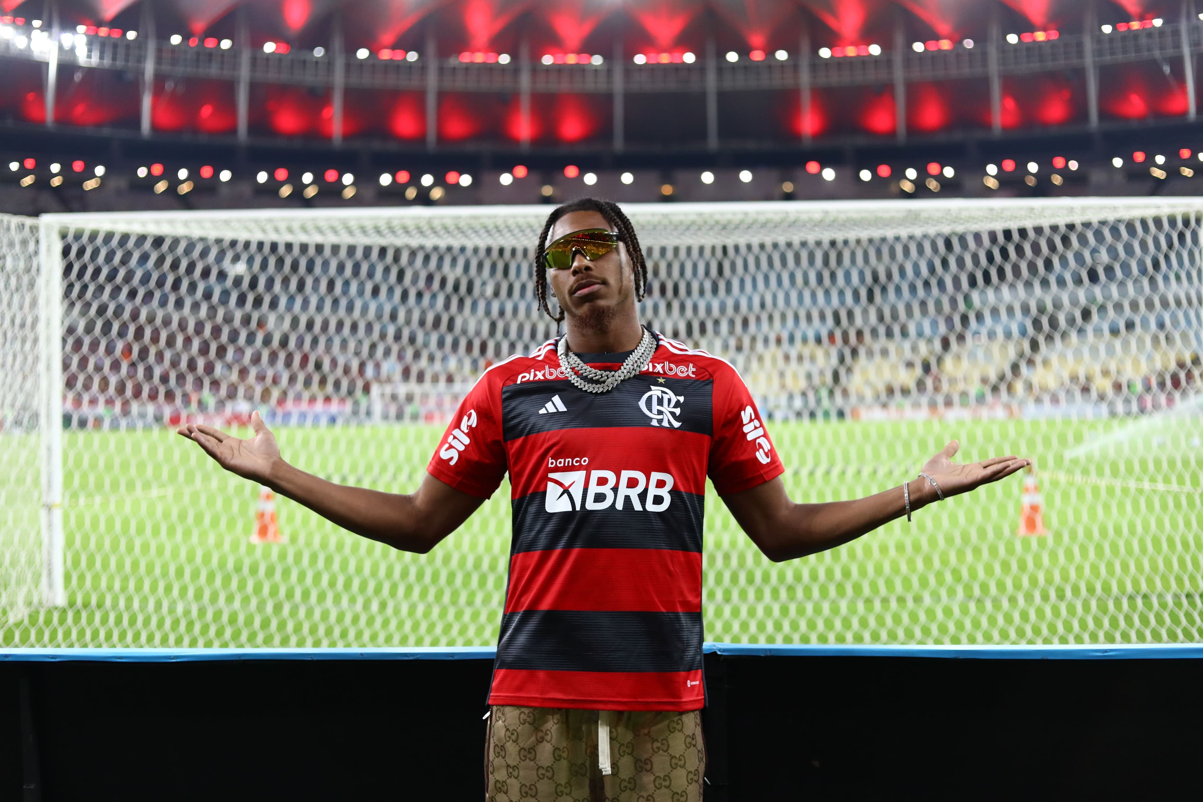 A man in a red and black shirt stands in front of a soccer goal in a stadium