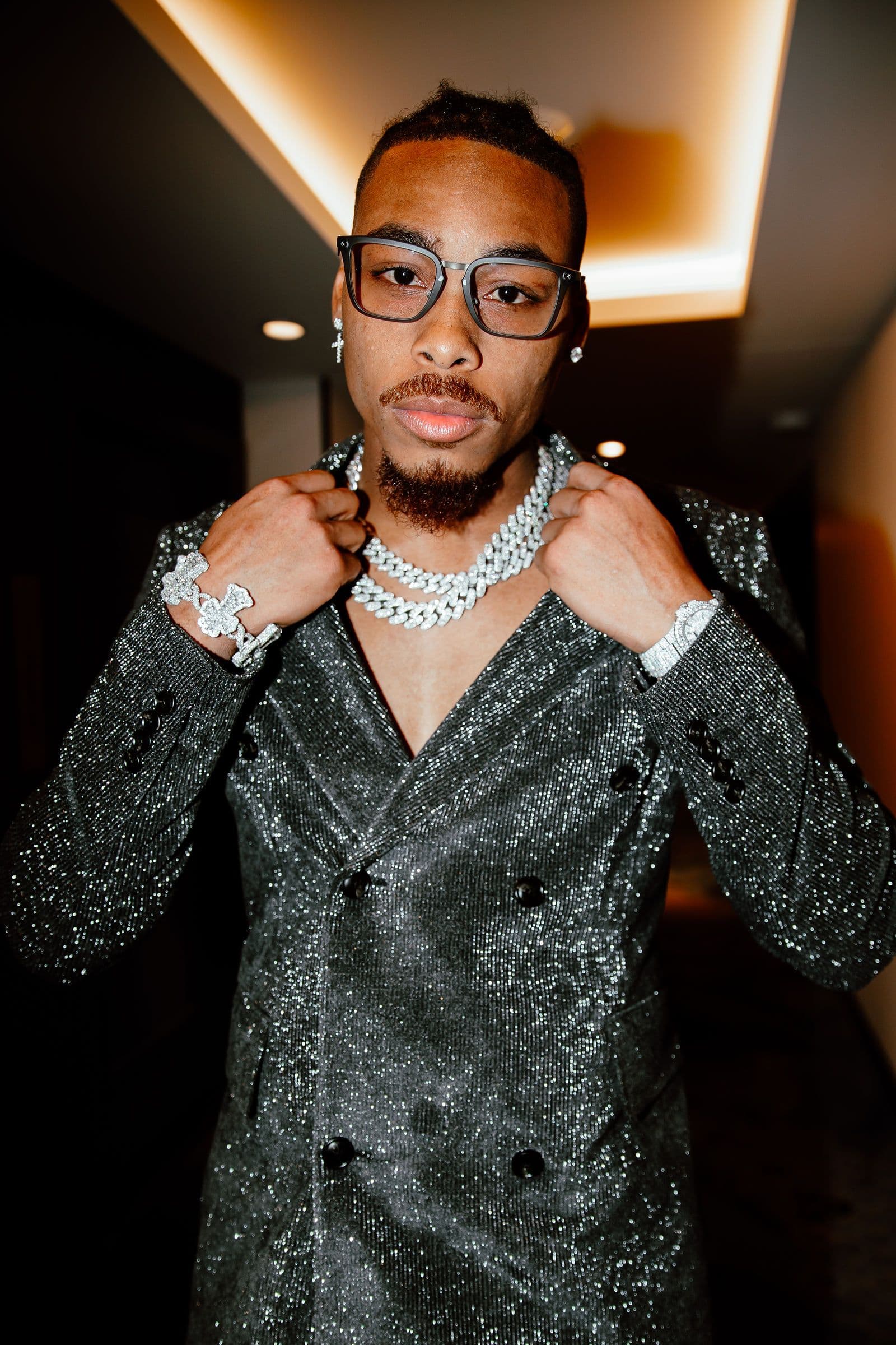 Justin Jefferson poses in a sparkly suit, glasses, and jewelry, looking at the camera