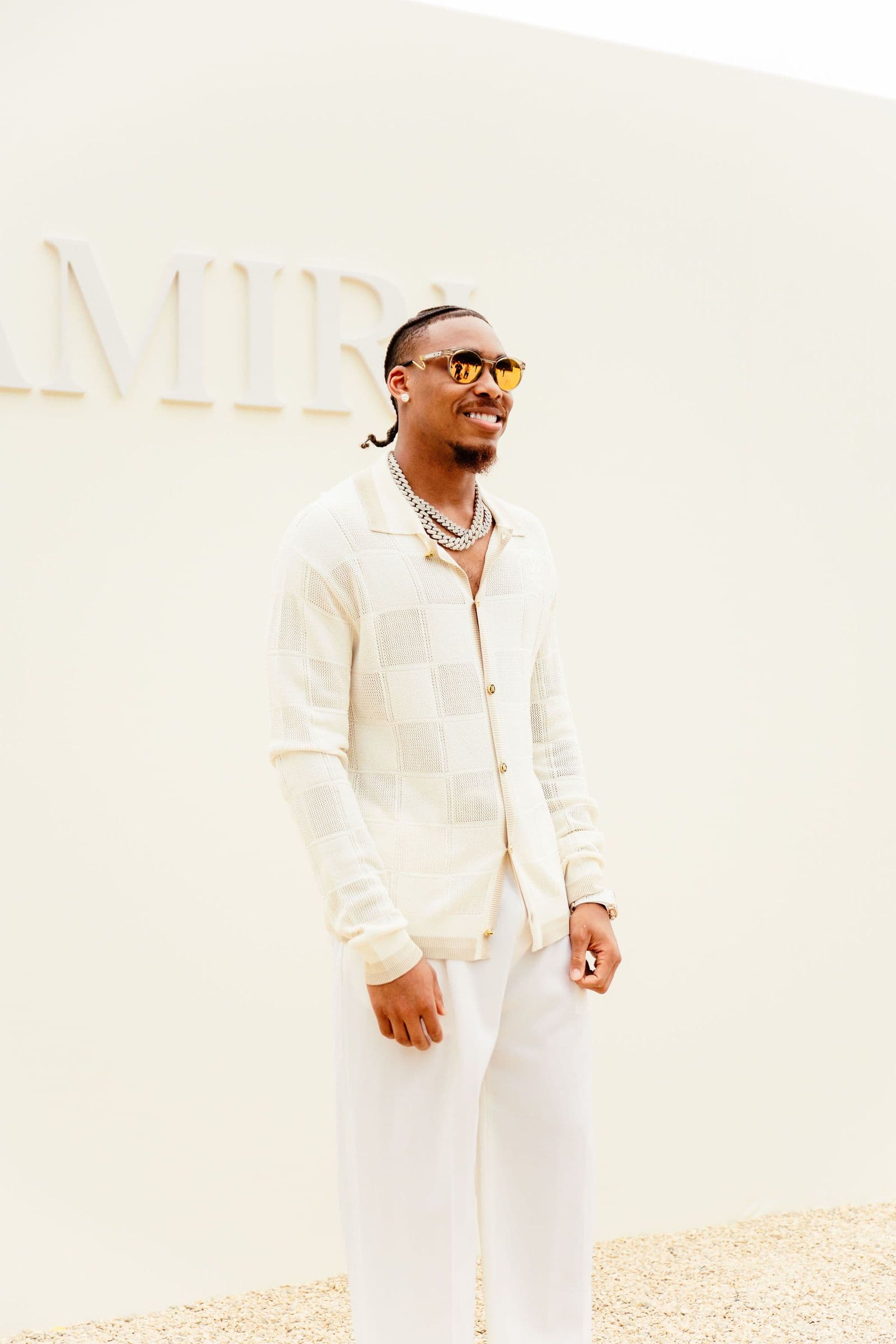 Justin Jefferson smiles, wearing a light outfit and sunglasses, standing against a light wall