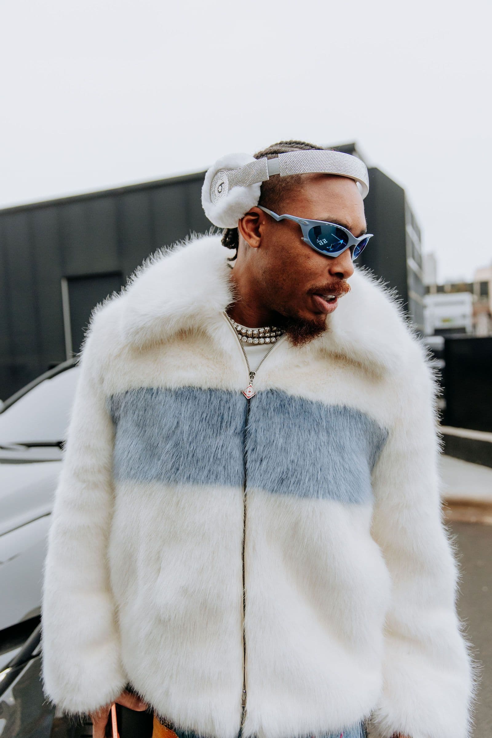 Justin Jefferson wears a white and blue fur jacket, blue sunglasses, and white headphones