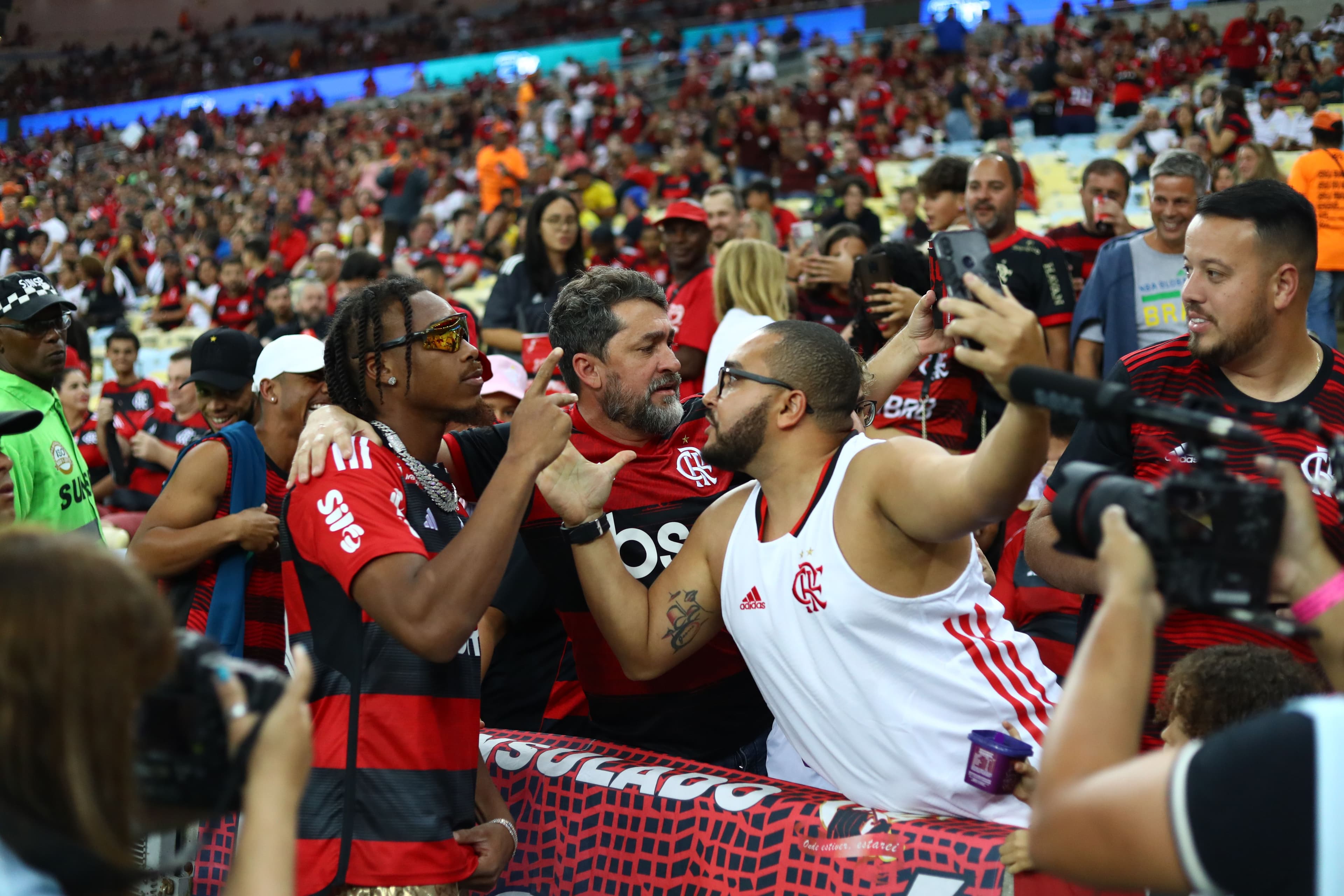 A person in a red and black shirt interacts with fans in a crowded stadium